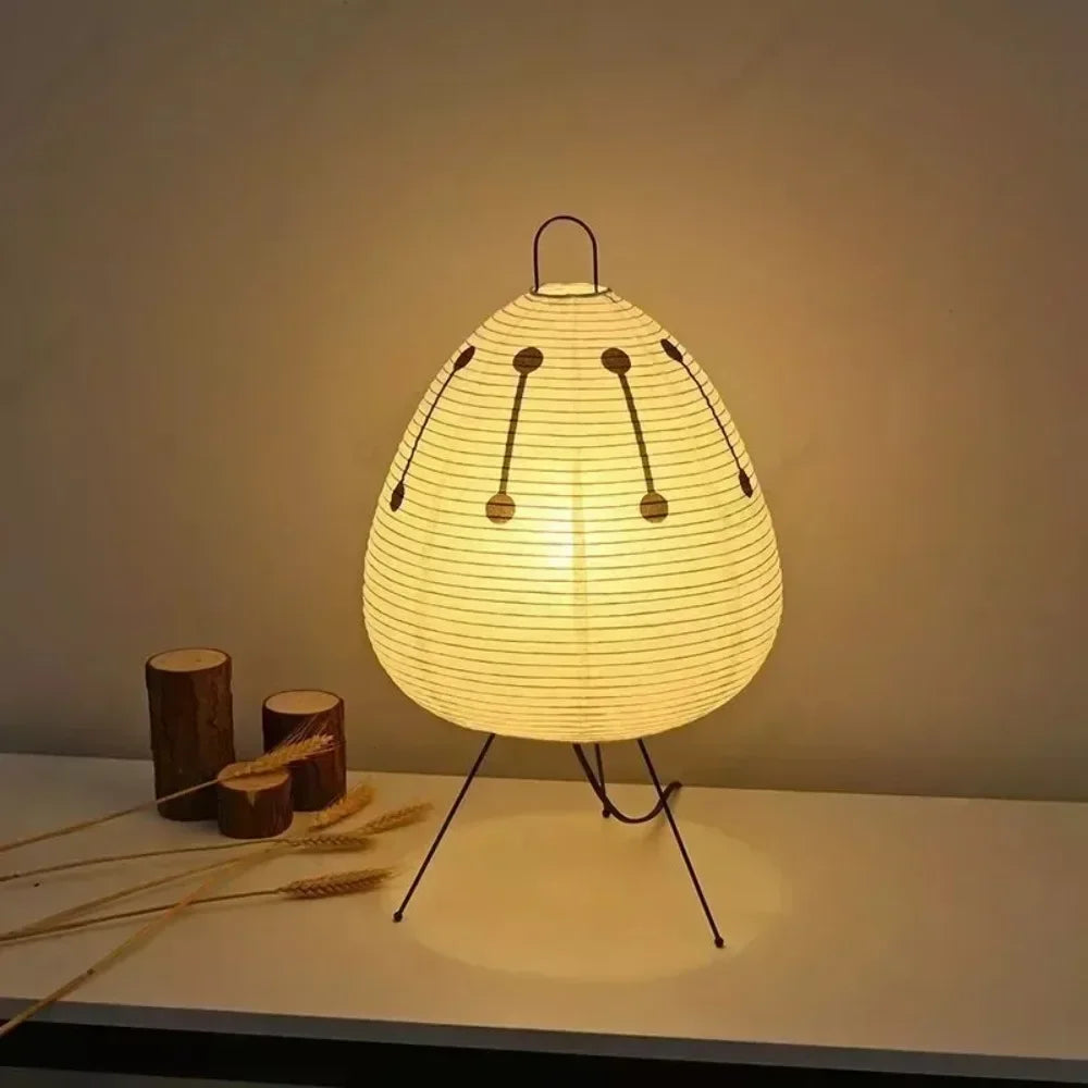 Lumae Sora printed paper lantern lamp on steel tripod legs, lit on a pale surface