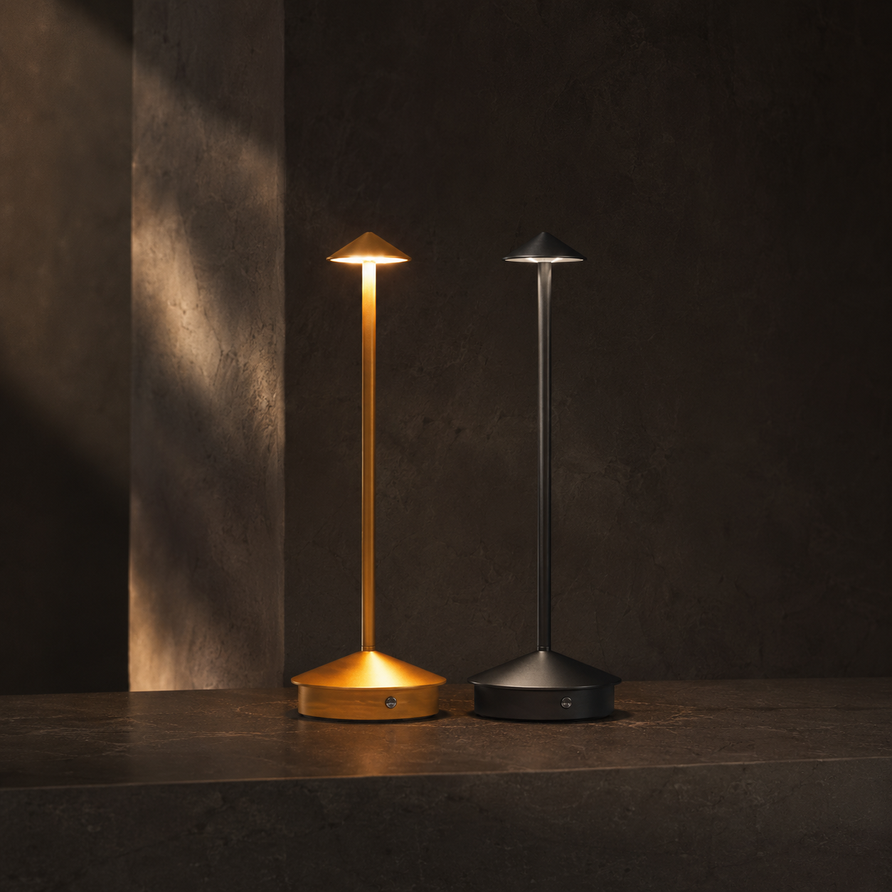 Lumae Garden cordless lamps in brass and graphite on dark stone at dusk