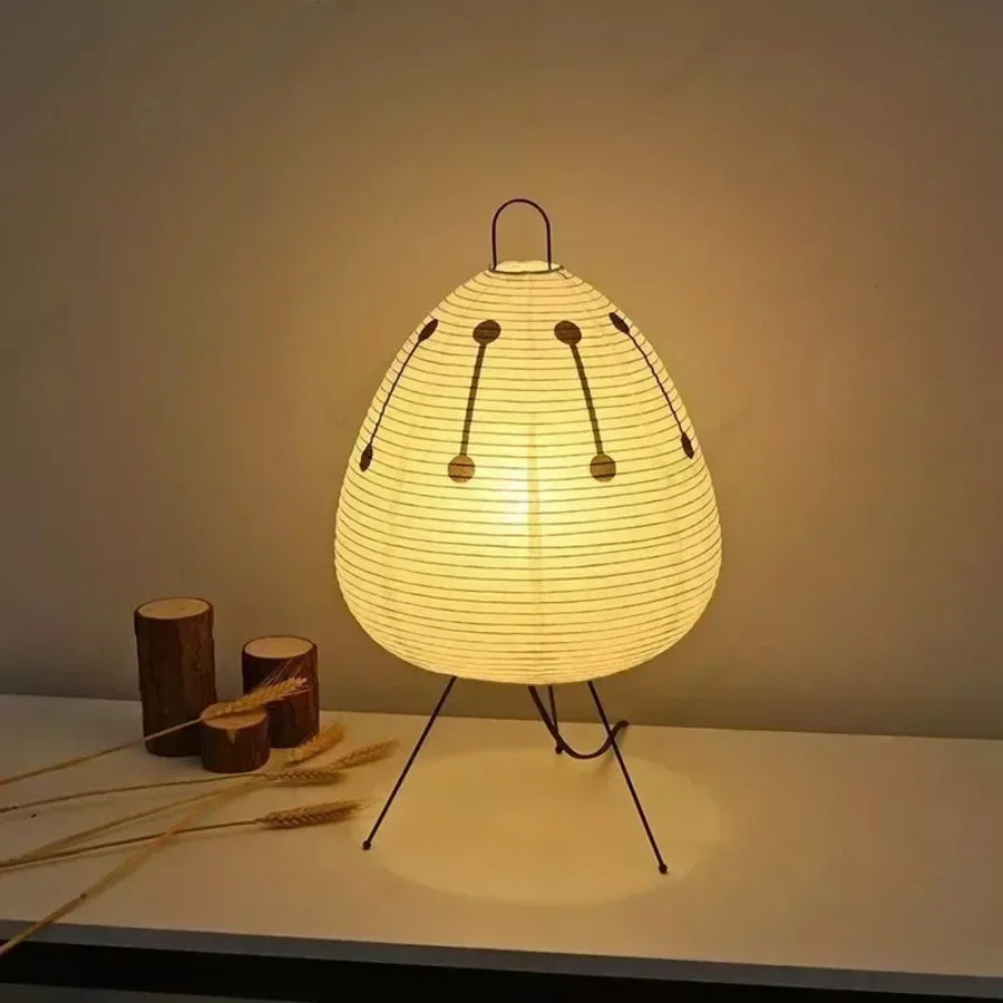 Lumae Sora printed paper lantern lamp on steel tripod legs, lit on a pale surface