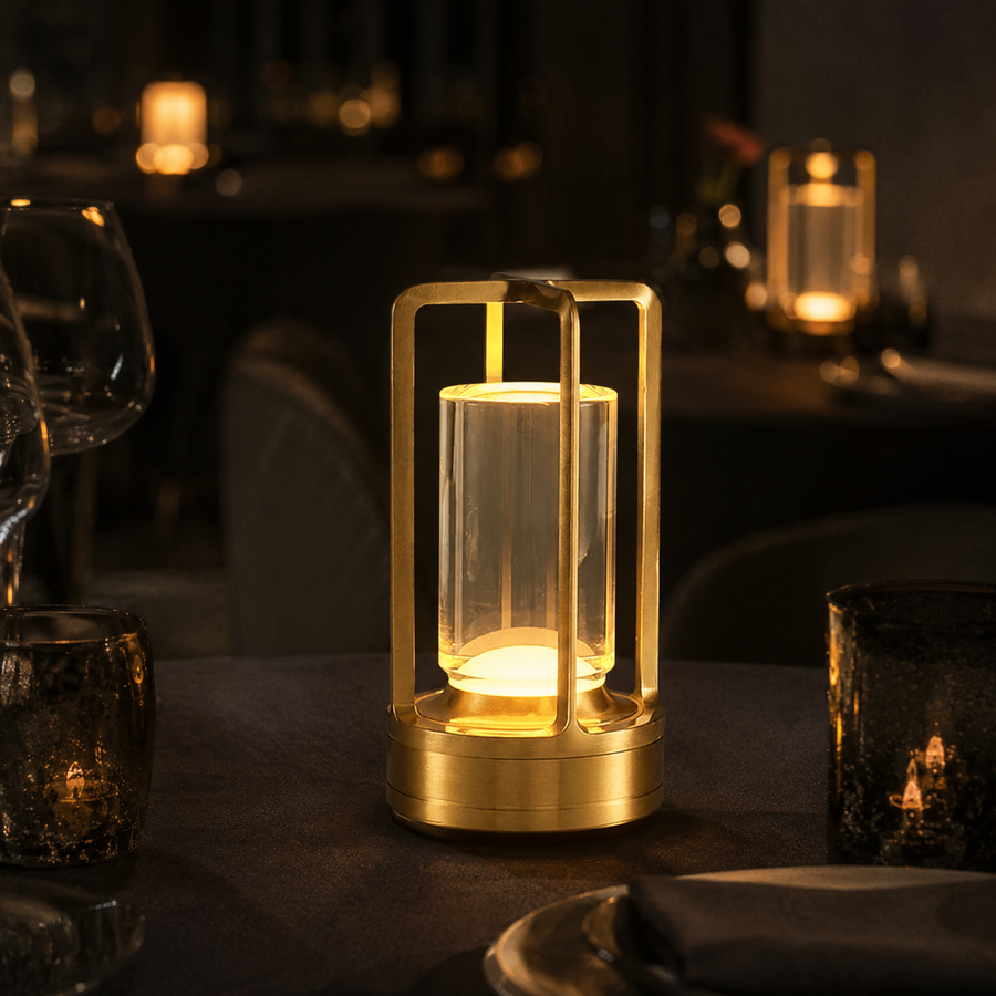 Lumae Marlow cordless lamp in gold lit on a dark restaurant table at night