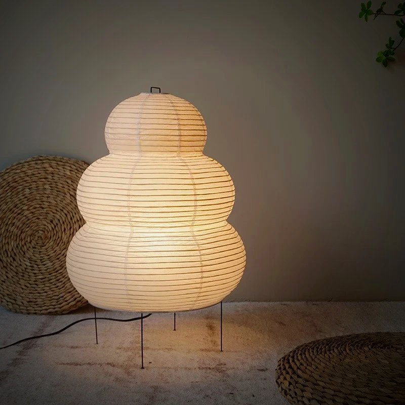 Mochi rice-paper table lamp glowing on a wood table beside woven mats